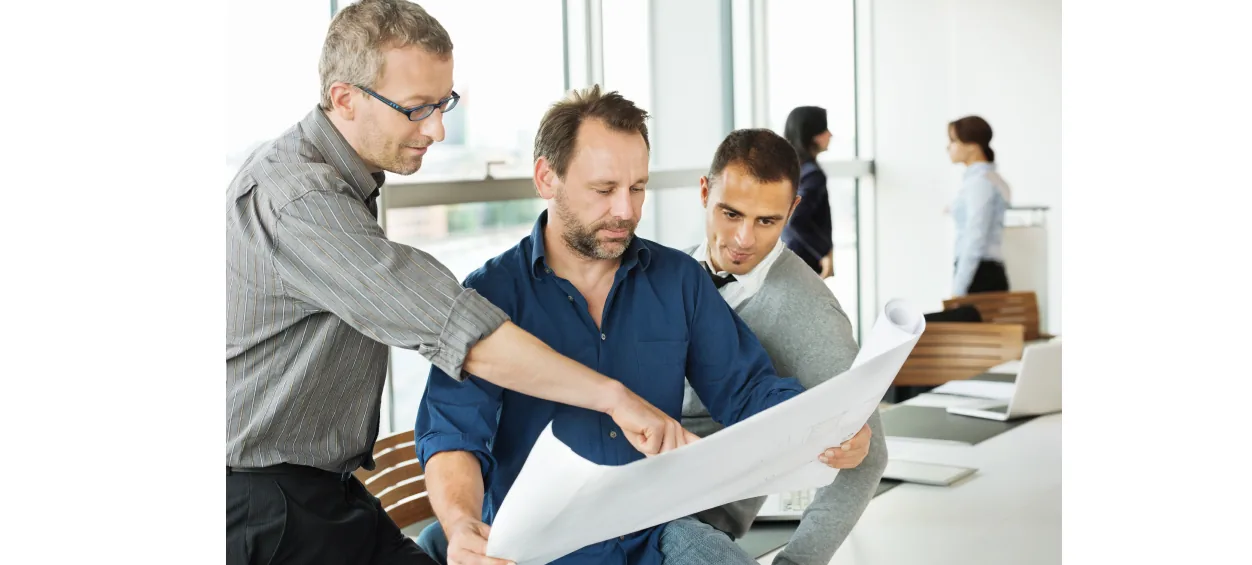 Drei Männer besprechen einen Plan in einem hellen Büro.
