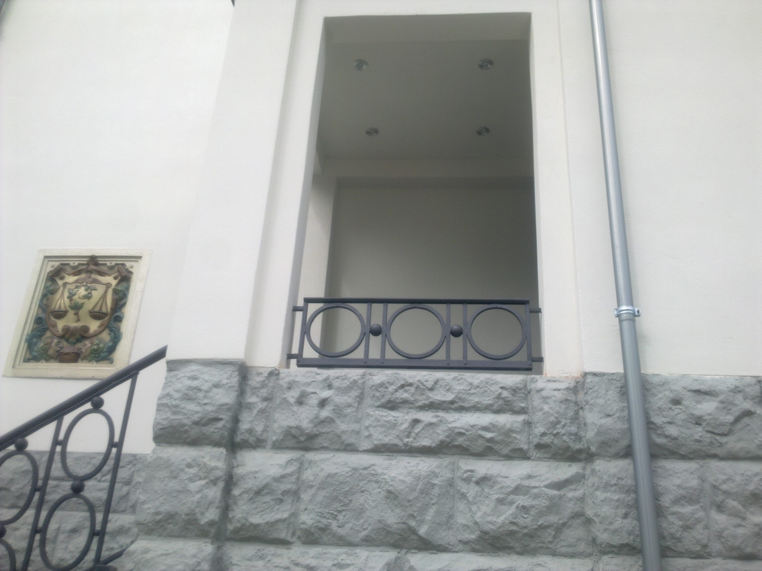 Anthrazitfarbene Fenstersicherung mit drei Kreisornamenten in einer Fensternische über einem Natursteinsockel, links das Treppengeländer im selben Ornament.