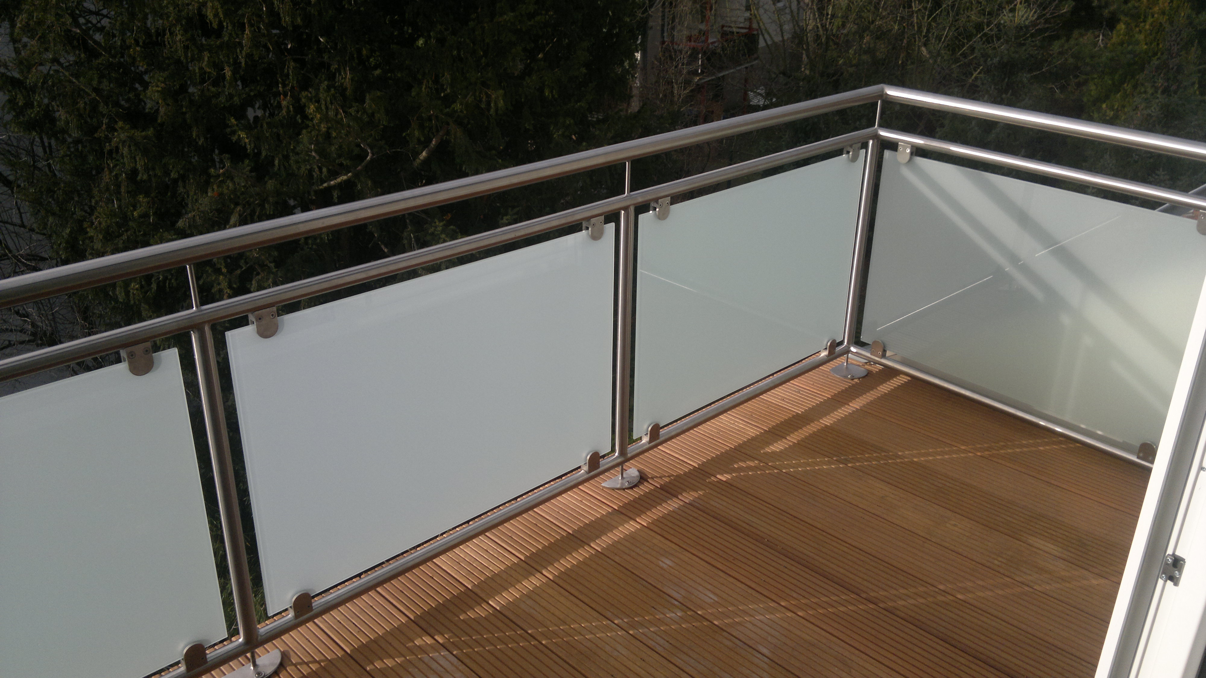 Edelstahl-Pfosten mit rundem Handlauf und Milchglasfüllung mit Punkthaltern auf dem Holzdeck einer Dachterrasse, von oben gesehen.