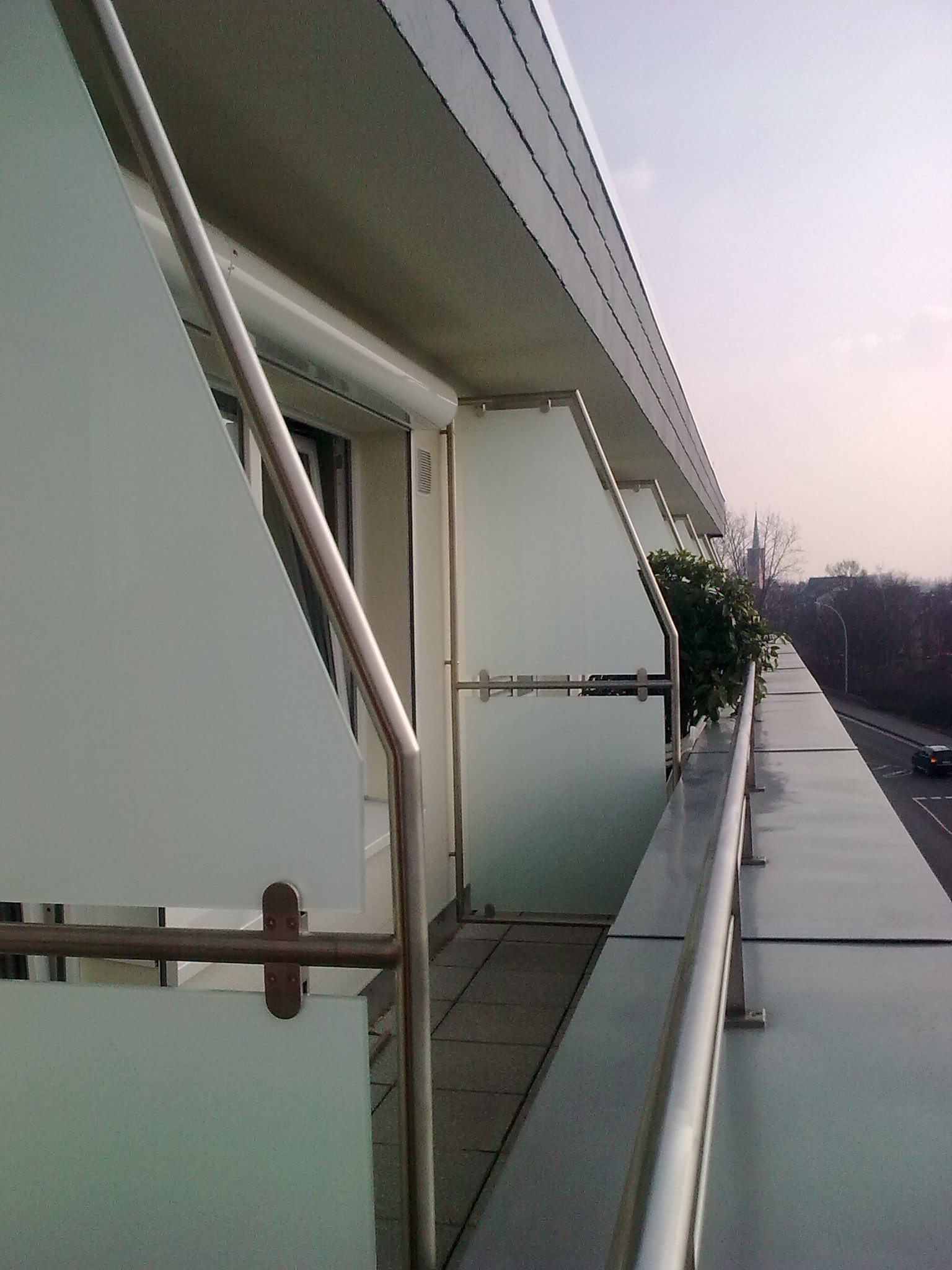 Durchlaufende Balkonbrüstungen mit Milchglasfüllung und rundem Edelstahl-Handlauf an einem Mehrfamilienhaus, mit Glas-Trennwänden zwischen den Balkonen.