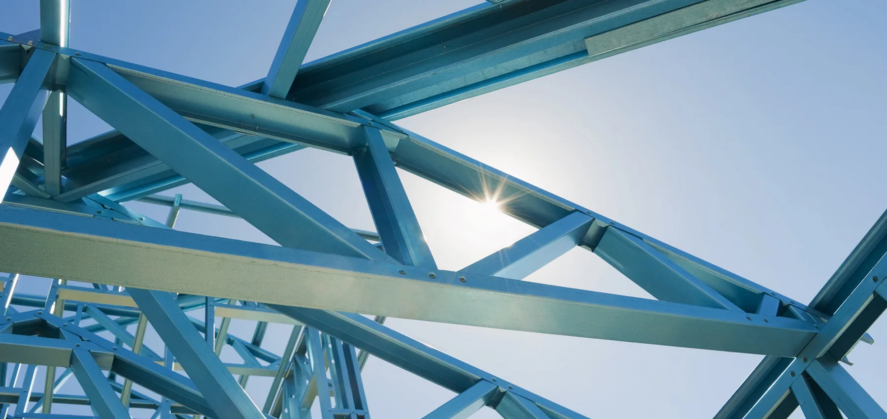 Blaues Stahlfachwerk vor dem Himmel, von unten gesehen, mit Sonne.